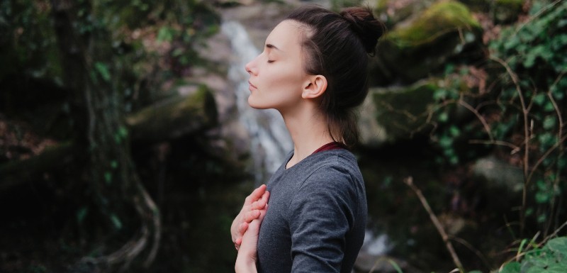 Femme devant une cascade qui ferme les yeux, les mains sur le coeur